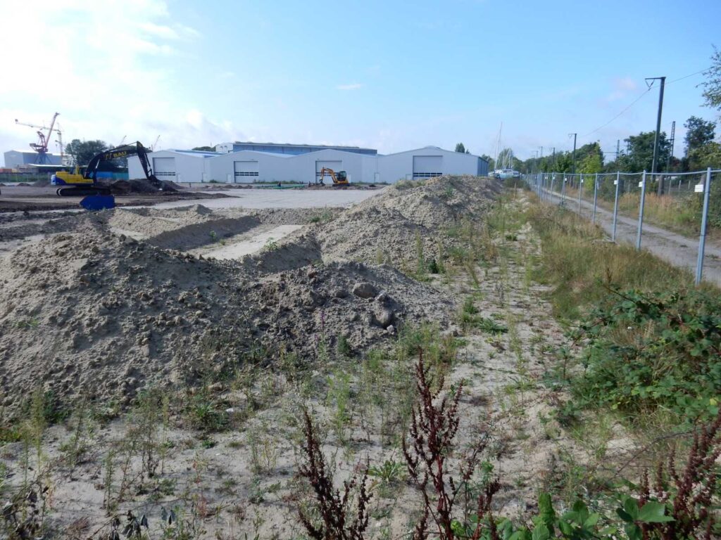 Baustelle mit Erdarbeiten, Bagger, Sandhaufen und Hallen im Hintergrund – transporttechniker.de