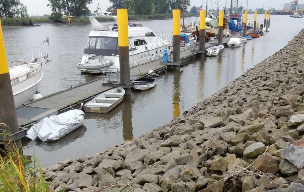 Hafen mit Booten, Stegen, gelb-schwarzen Pollern und Steinbefestigung am Ufer – transporttechniker.de
