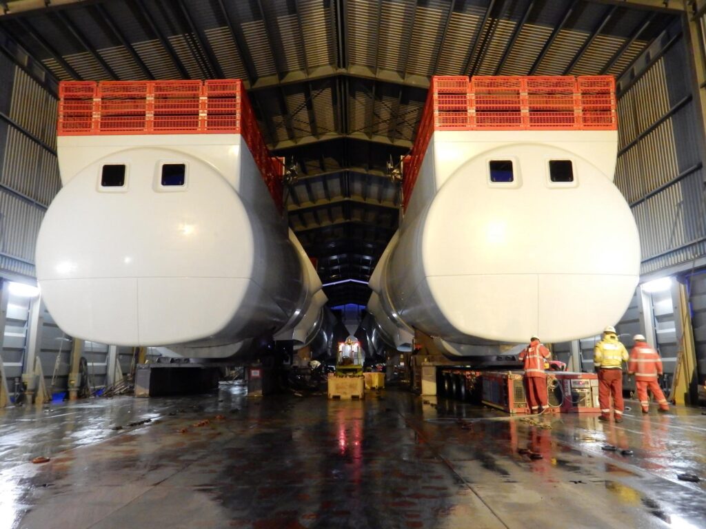 Montage von zwei Windkraft-Gondeln (Nacelles) in einer Industriehalle mit Arbeitern – transporttechniker-de