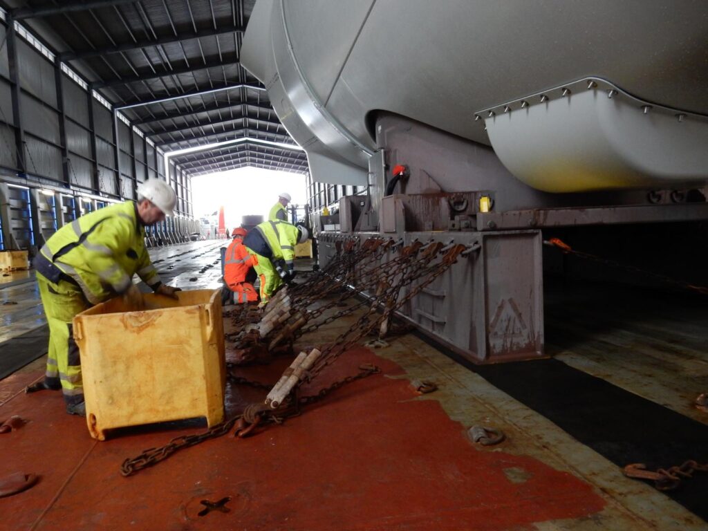 Montage Ladungssicherung eines Sattels (Support) für eine Windkraft-Gondel mit Ketten in einer Industriehalle – transporttechniker-de