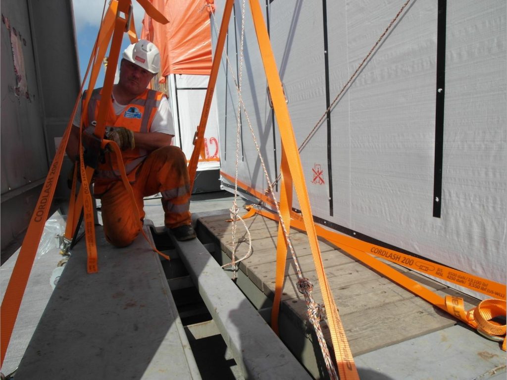 Foto eines Arbeiters in orange Sicherheitskleidung bei Sicherungsarbeiten mit CORDLASH 200 Gurten für Schwerlast-Sicherung