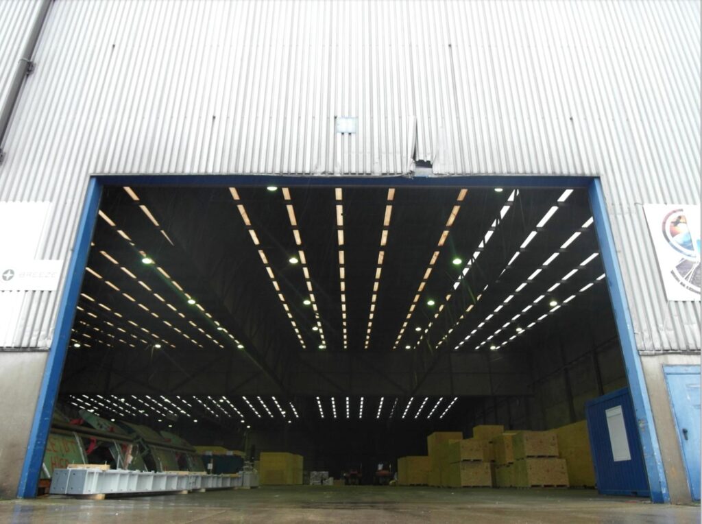 Große Industriehalle mit geöffnetem Hallentor und beleuchteter Lagerfläche für Logistik, Maschinenbau und Schwerlastlagerung
