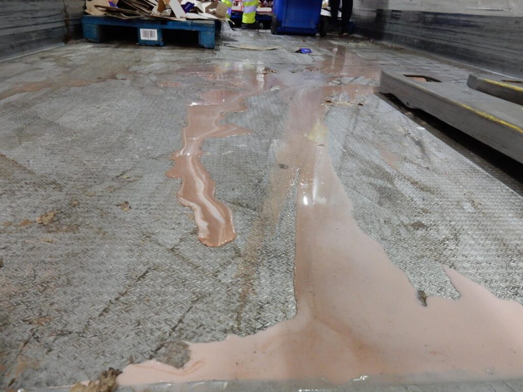 Verschmutzte LKW-Ladefläche mit Milchprodukten-flüssig, Pappresten und Müll – Metallboden mit Rutschgefahr.