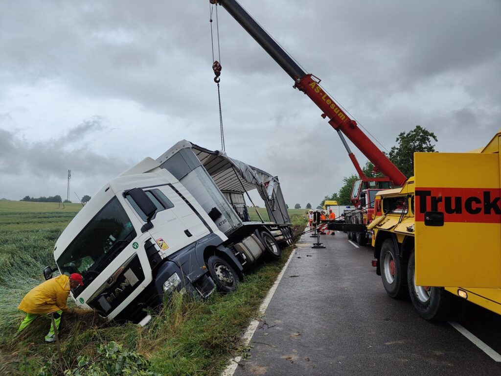Umgestürzter LKW wird von Kran (AS Lesum) und Bergungsfahrzeug (Truck Service) auf nasser Landstraße aufgerichtet – Arbeiter in Warnwesten sichern die Szene.