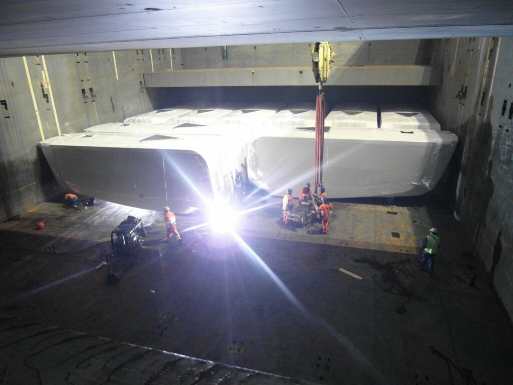 Foto vom Schwerlastumschlag im Schiffsinneren: Verpacktes Gut wird mit Kran und Arbeitern bei einfallendem Sonnenlicht bewegt