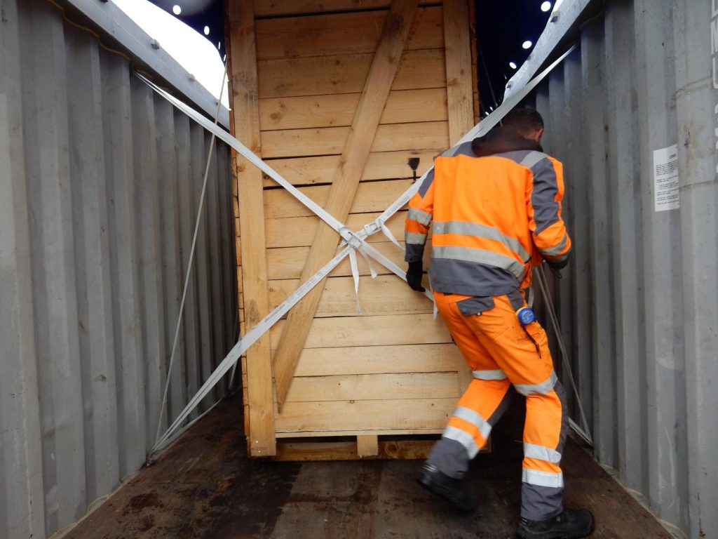 Arbeiter in Warnweste sichert Holzkiste im Container – transporttechniker.de