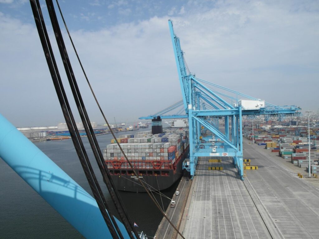 Foto eines Containerschiffs (Mærsk) im Hafen mit blauen Container-Kranen von APM Terminals und gestapelten Containern auf dem Kai beim Schwerlastumschlag