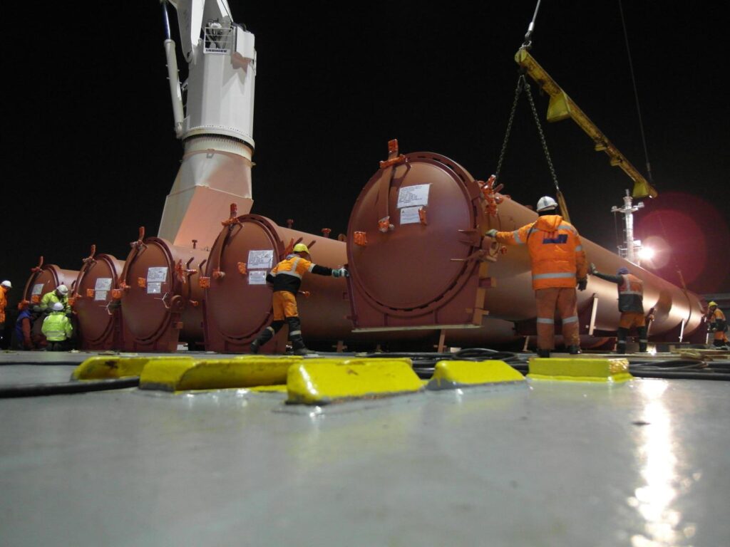 Foto von Schwerlast-Tanks/Behältern beim nächtlichen Umschlag mit Kran und Arbeitern in orange Sicherheitskleidung
