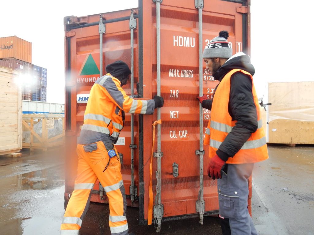 Foto von zwei Arbeitern in orange Sicherheitskleidung beim Öffnen der Türen eines HDMU-Hyundai-Containers mit sichtbaren technischen Daten