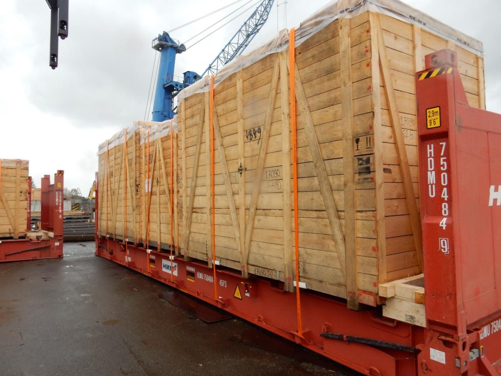 Holzkisten mit orangefarbenen Spanngurten auf Flatracks im Hafen gelagert – transporttechniker.de