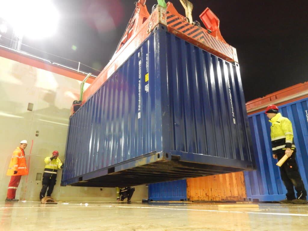 Kran hebt blauen Container auf Schiff im Hafen bei Nacht – transporttechniker.de