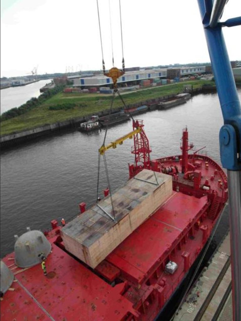 Kran lädt riesige Holzkiste als Schwerlast auf Schiff – transporttechniker.de