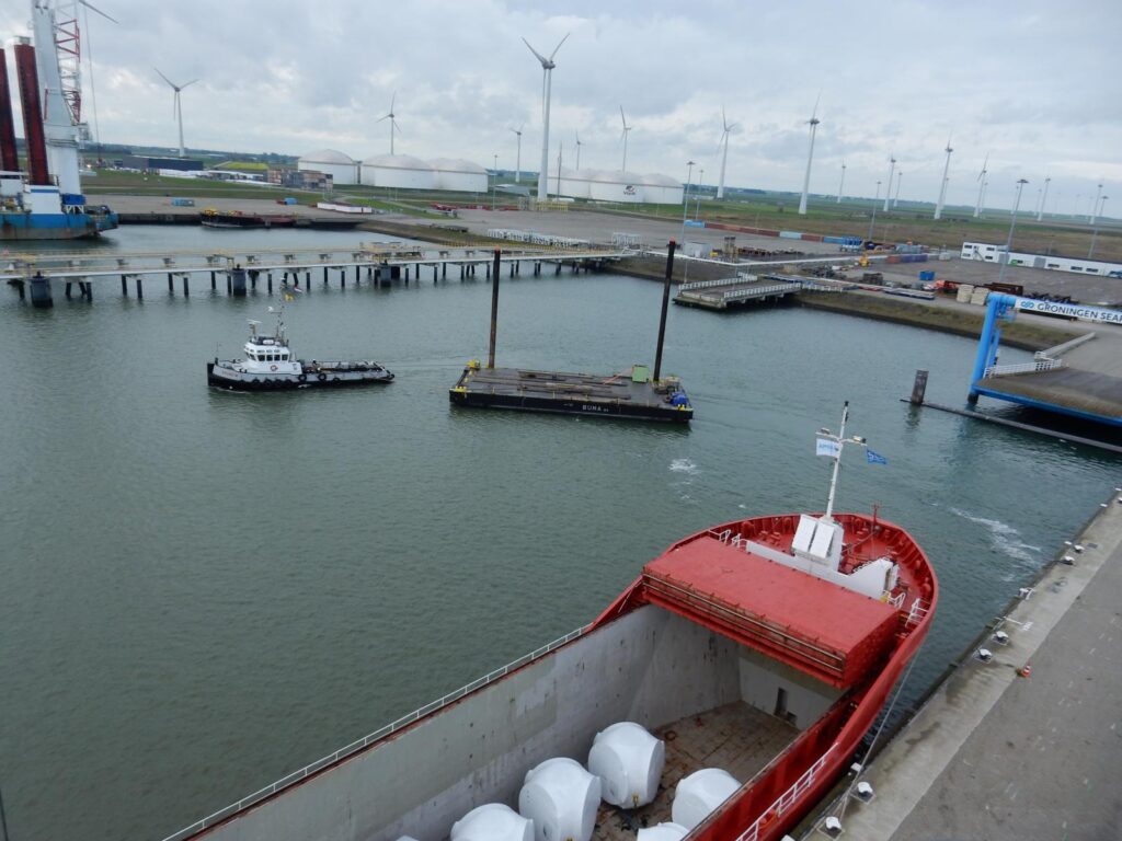 Schlepper zieht Schiff mit Windkraft-Fundamenten im Hafen – transporttechniker.de