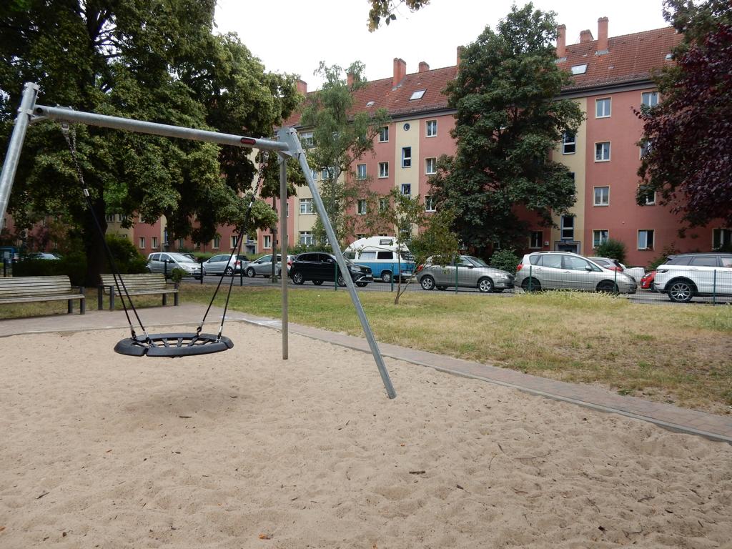 Spielplatz in der Dusekestraße, Berlin – Schaukel mit Sandfläche, Bänken und Wohnhäusern im Hintergrund – transporttechniker.de