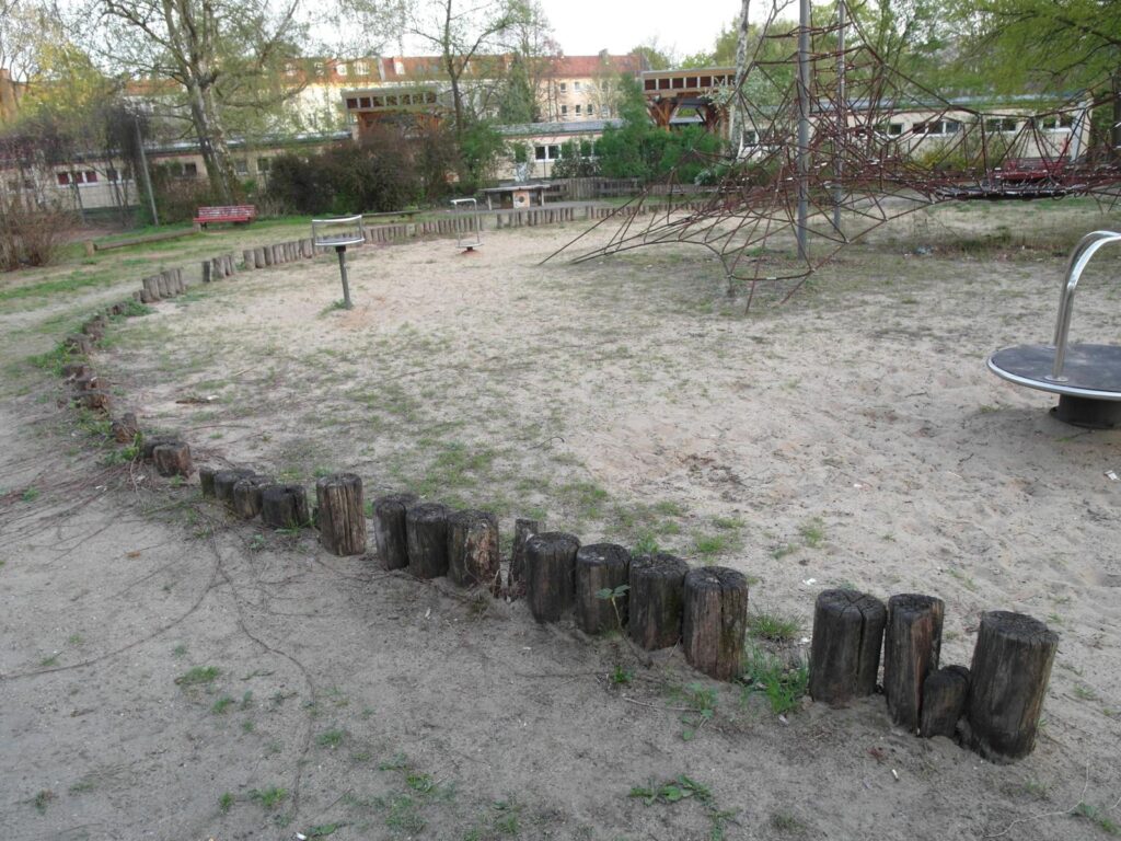 Spielplatz in der Dusekestraße, Berlin – Ist-Zustand mit Sandfläche, Baumstammbegrenzung und Spielgeräten – transporttechniker.de