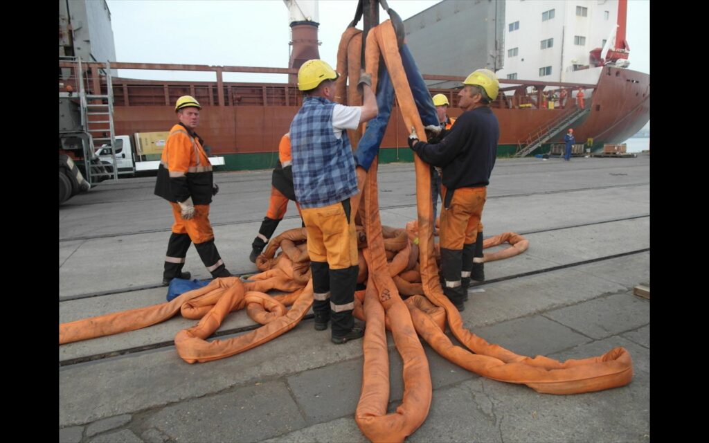 Anschläger bereiten Anschlagmittel und Rundschlingen für die Heavy-Lift-Verladung einer Schwerlastkomponente im Hafen vor. Technische Ladevorbereitung und Transport Engineering durch transporttechniker.de
